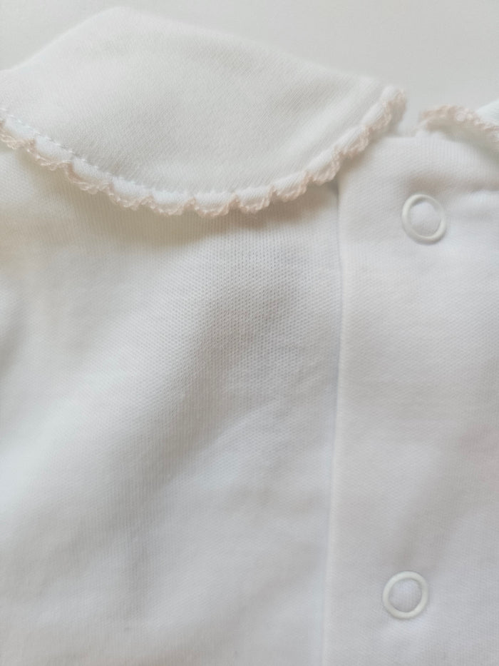 Close-up of a white baby outfit with lace trim on a light background