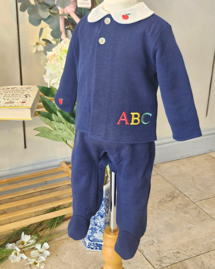 A navy blue baby footed sleeper with a white collar and colorful embroidered letters 'ABC' on the chest, displayed on a mannequin torso.
