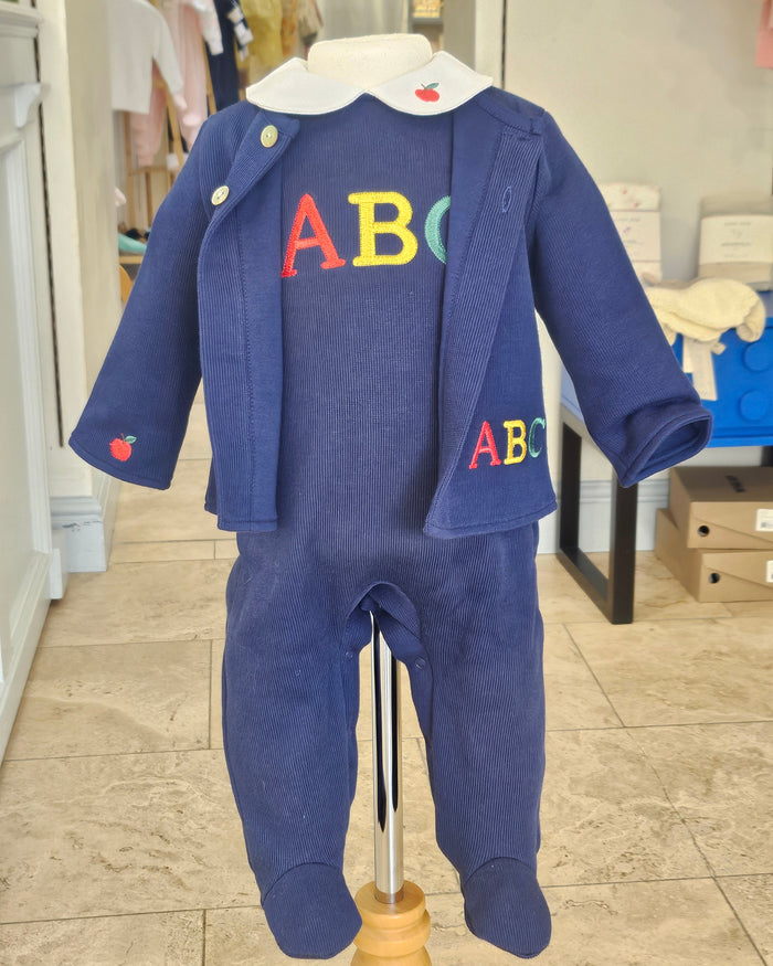 A navy blue baby jumpsuit with colorful embroidered letters 'ABC' on the chest and a small red apple detail on the sleeve, displayed on a mannequin in a retail store.