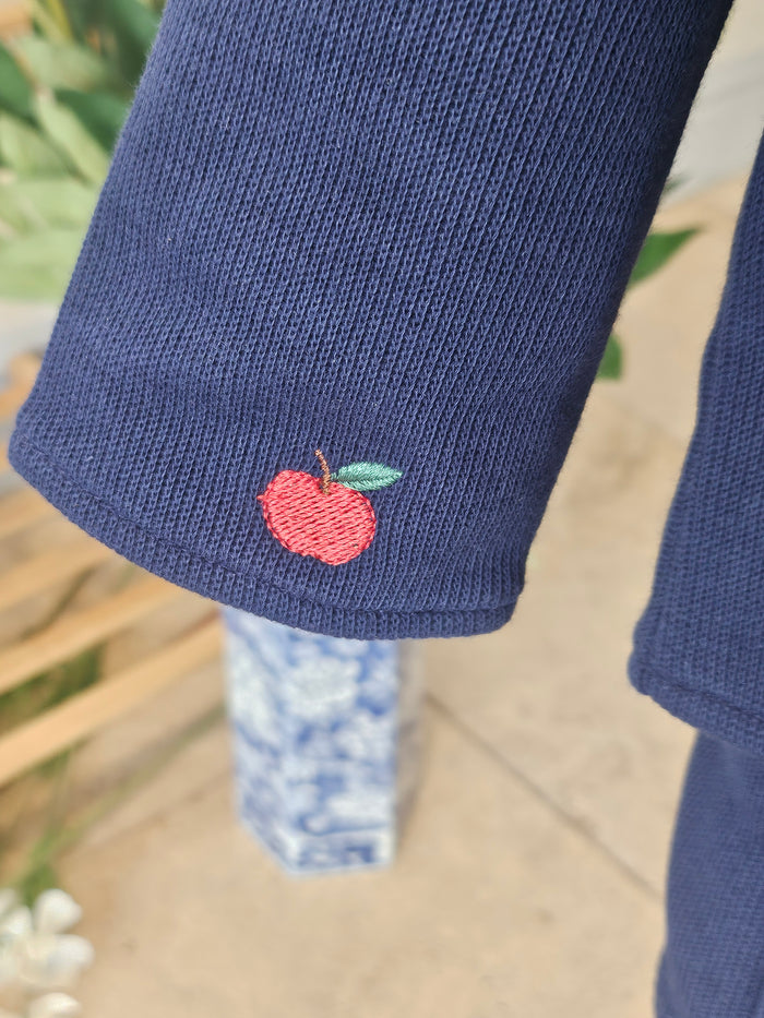 Close-up of a navy blue ribbed knit sleeve featuring a small embroidered red apple with a green leaf on the cuff.