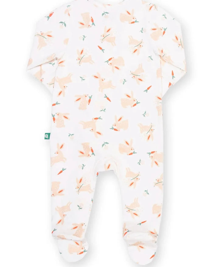 A baby footed sleeper in white with a repeating pattern of light orange rabbits and carrots, shown against a plain white background.