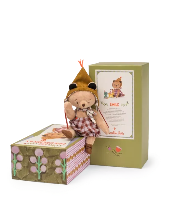 Stuffed teddy bear in a hat and dress sitting on a box with a green gift box in the background.