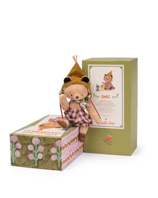 Stuffed teddy bear in a hat and dress sitting on a box with a green gift box in the background.