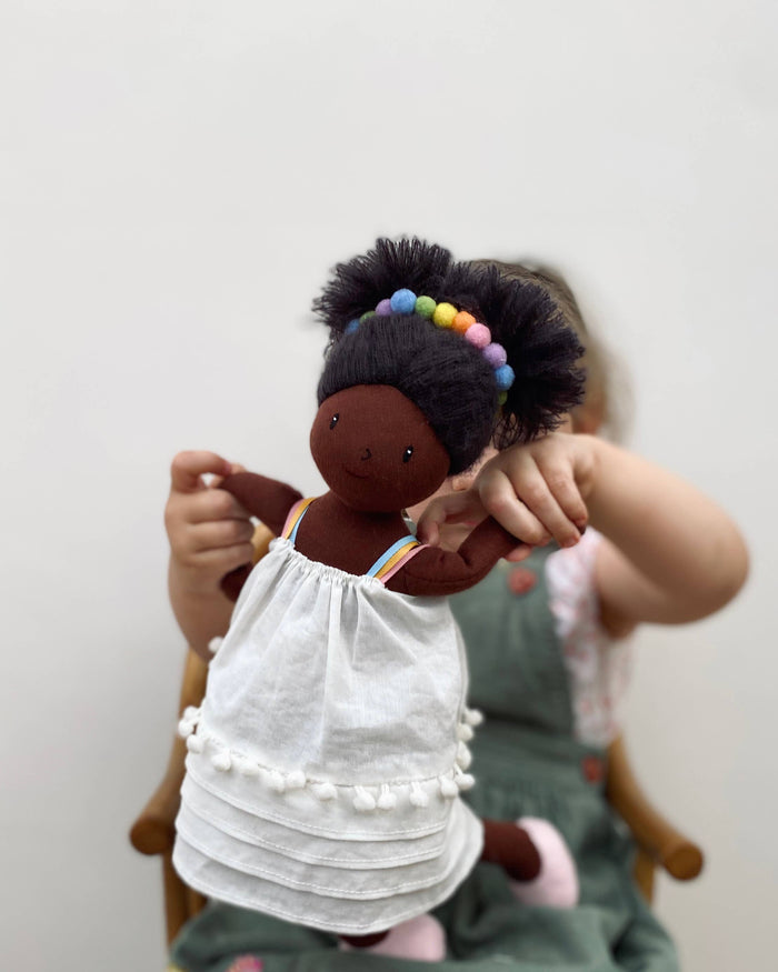 Child holding a doll with a white dress against a plain background