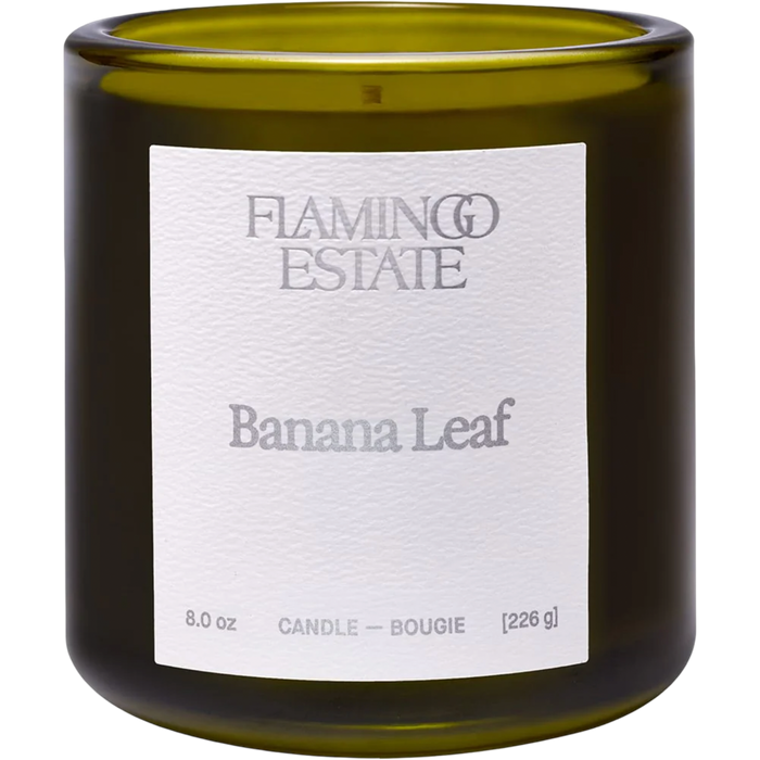 An 8.0 oz glass candle in a dark olive green jar with a white paper label reading 'FLAMING ESTATIE Banana Leaf'.