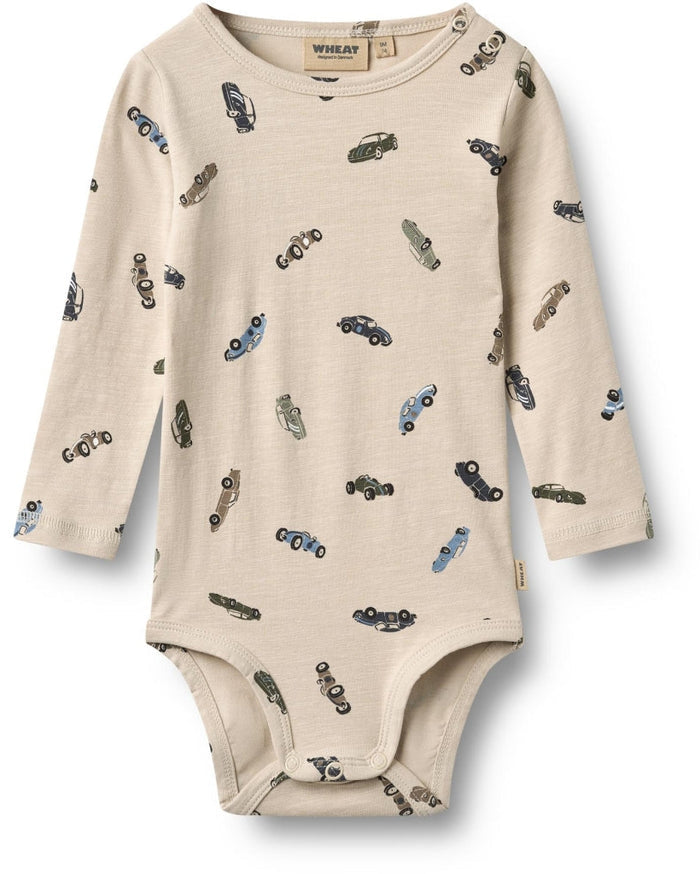 A long-sleeve baby bodysuit in cream-colored cotton muslin fabric, featuring an all-over print of vintage cars in blue, gray, and black. The brand name 'WHALEY' is visible on the inner neck label.