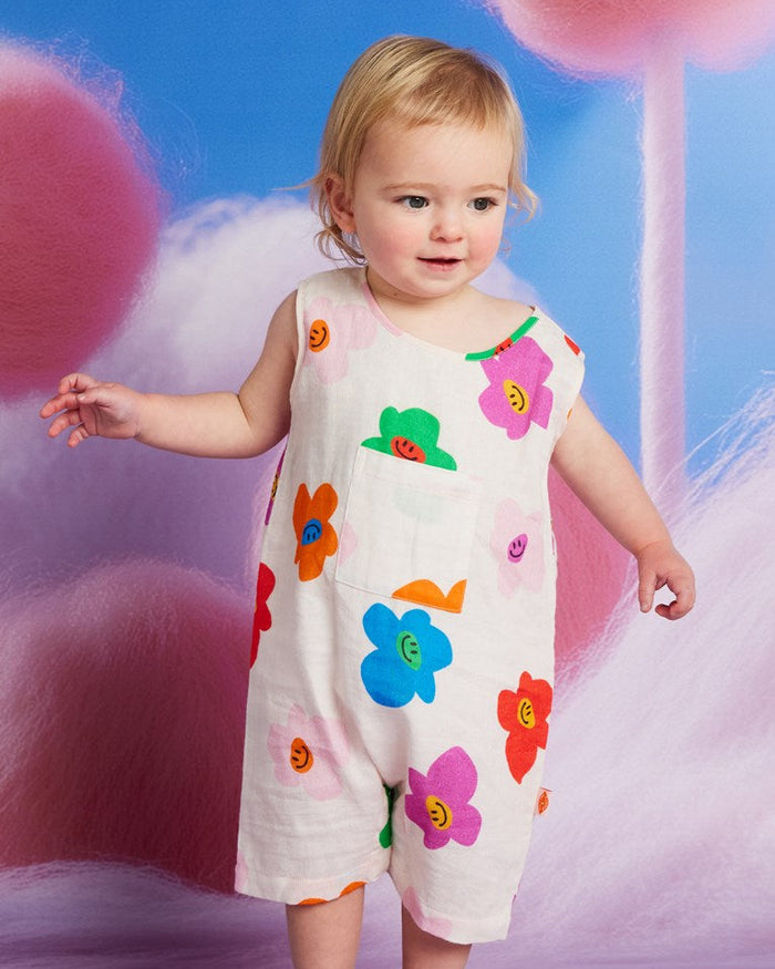 Child wearing a colorful floral dress against a whimsical background with fluffy pink clouds and a blue sky.