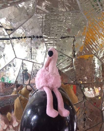 Pink flamingo toy on a black bottle against a reflective mirror background