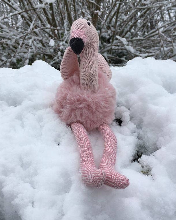 Knitted flamingo toy in the snow with a snowy background