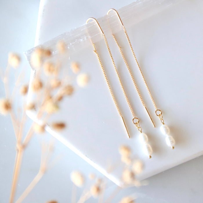 Two gold necklaces on a white surface with dried flowers.