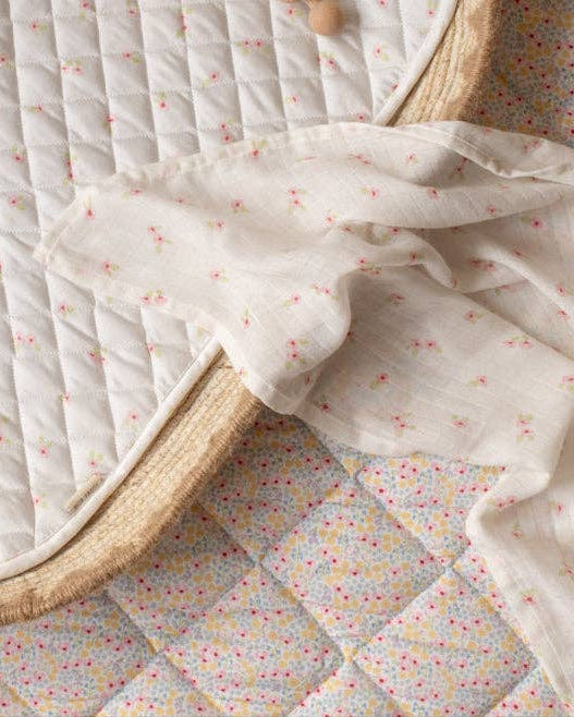 Floral-patterned quilt draped over a wicker chair on a checkered floor.