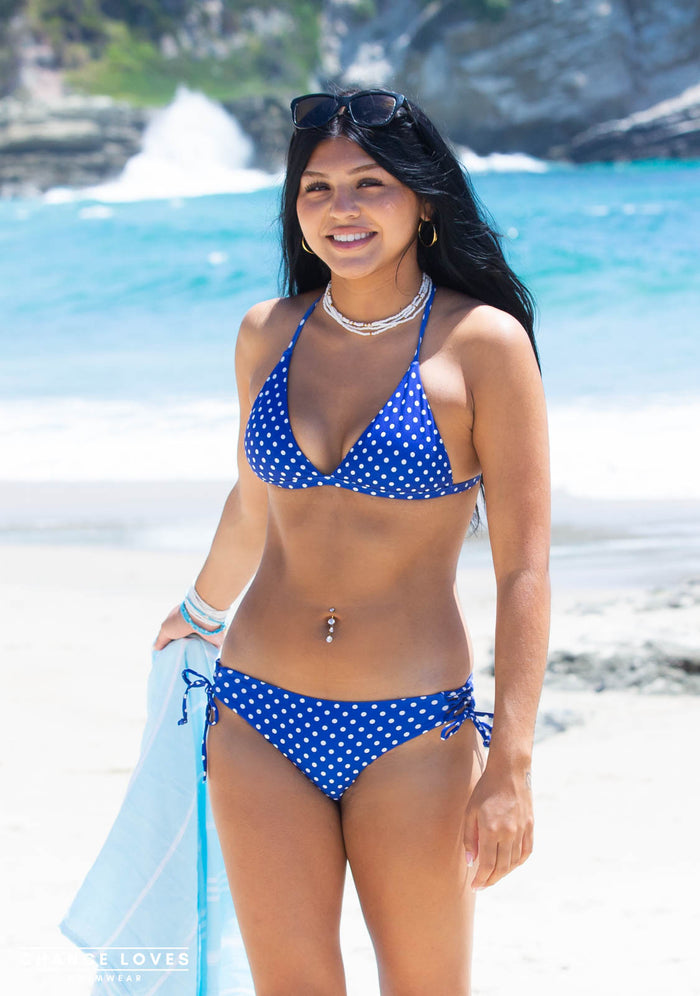 17 year old girl in a Chance Loves blue polka dot bikini standing on a beach with ocean in the background