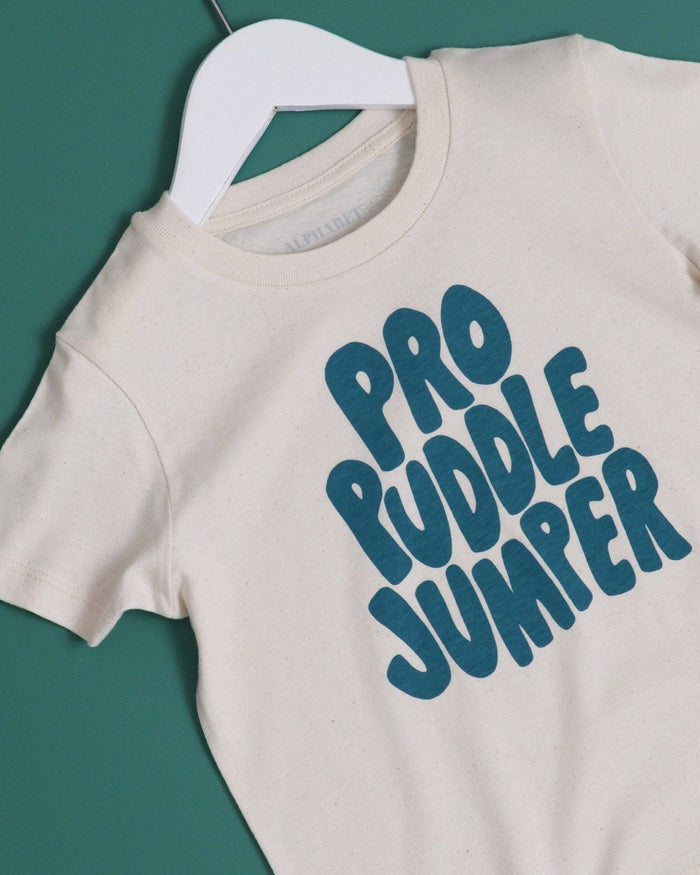 Beige t-shirt with 'Pro Puddle Jumper' text on a hanger against a green background
