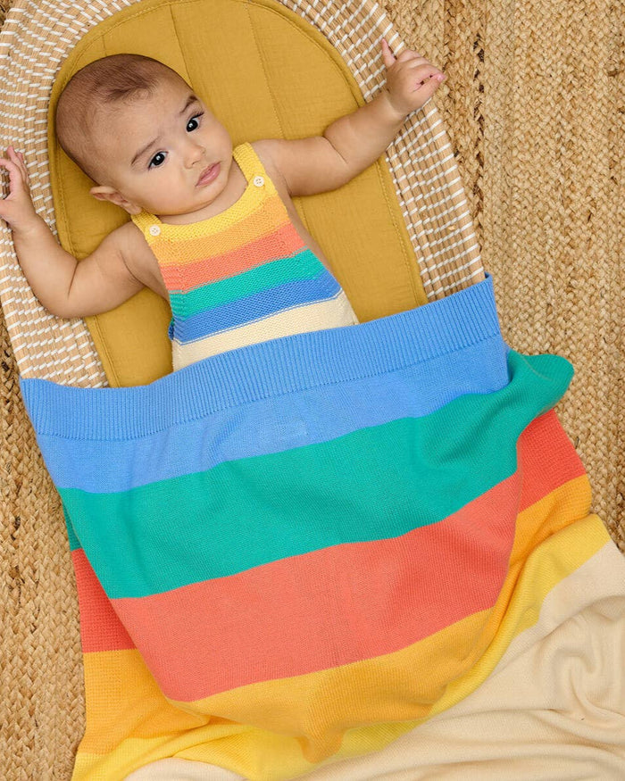 Baby in a colorful striped outfit lying on a woven surface