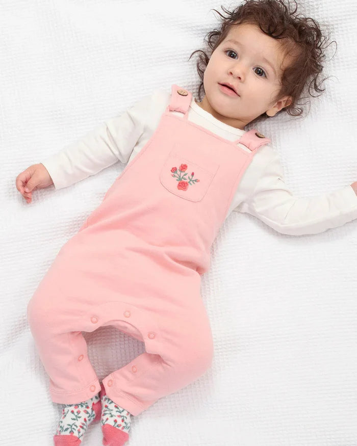 Baby wearing a pink dungaree with a floral design on a white background