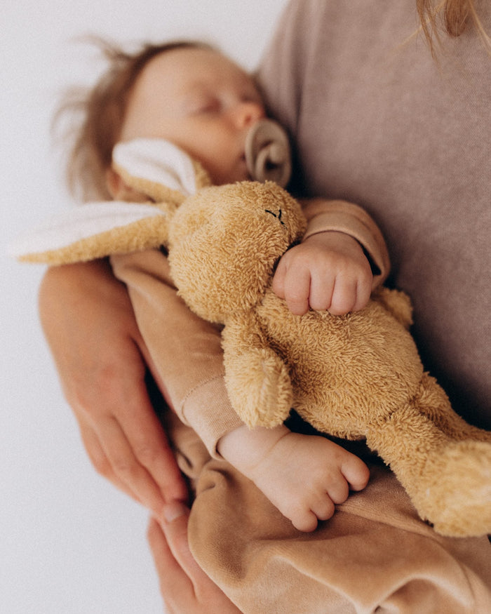Baby holding a brown teddy bear with a blurred background