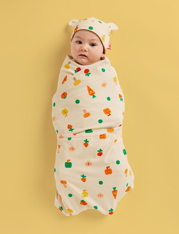 Baby swaddled in a colorful blanket with a yellow background