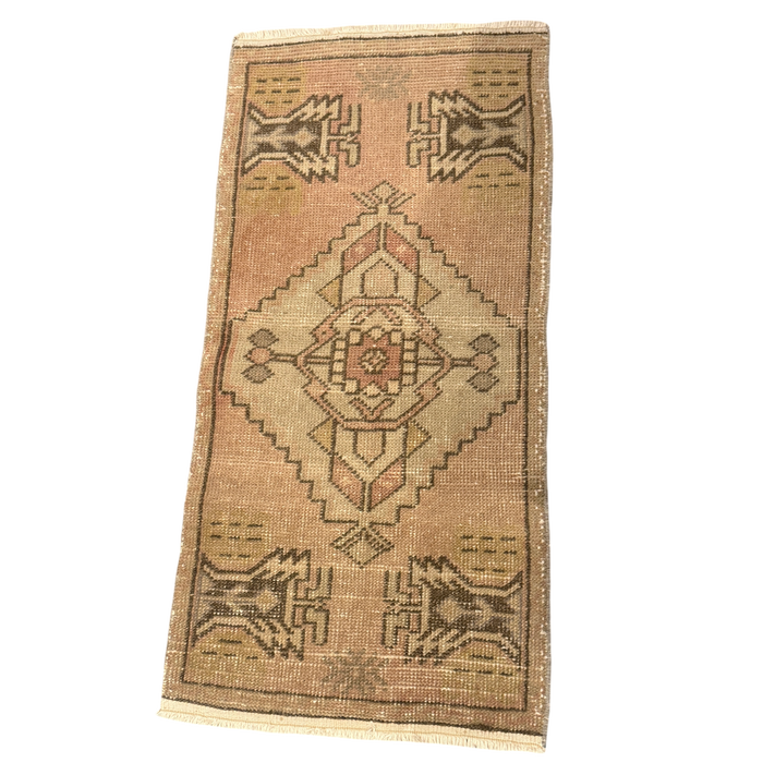 Dusty coral mini rug with a stepped cream medallion, mirrored brown geometric motifs at each end, a narrow border, and cream fringe.