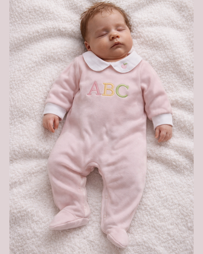 Baby in a pink outfit with 'ABC' on a white blanket
