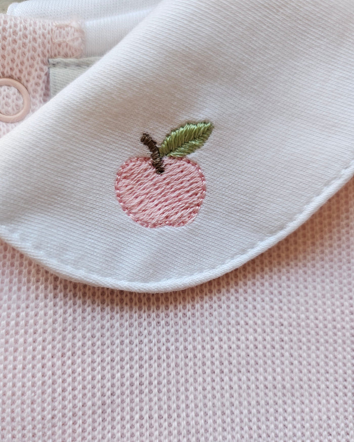 White fabric with pink embroidered peach and green leaves on a textured pink background