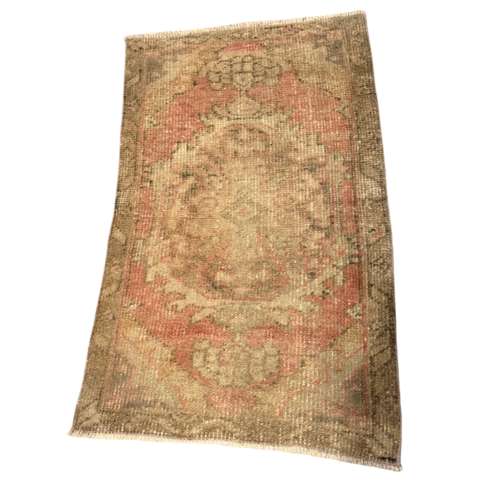 Faded rose and cream mini rug with an ornate floral medallion, olive-toned border, pronounced surface wear, and short cream fringe.