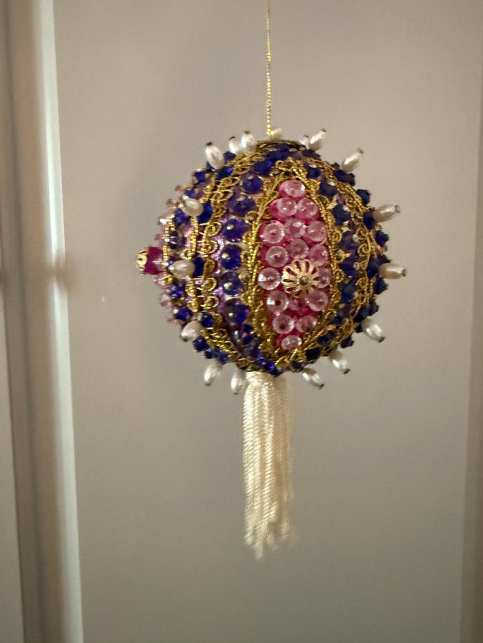 Vintage round ornament with purple beads, pink sequins, gold-tone braid, pearl-look accents, and an ivory tassel hanging from a gold cord.