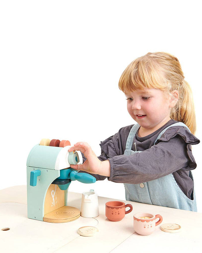 Child playing with a toy coffee machine and cups on a white background