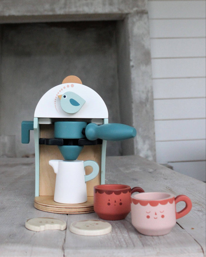 Children's toy coffee maker set with cups and a bird design on a wooden surface.