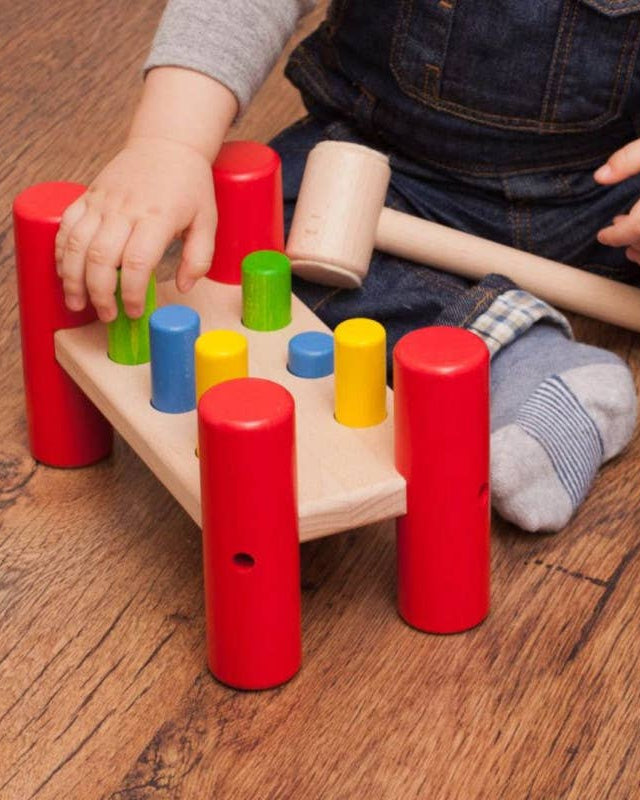 Child playing with a colorful wooden peg puzzle on a wooden floor.
