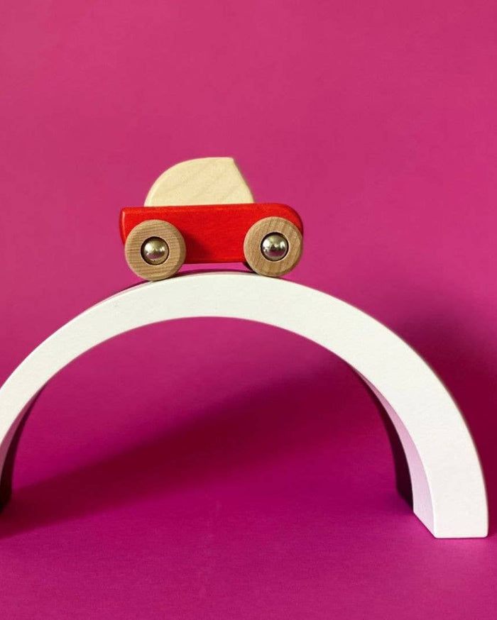 Wooden toy car on a white arch against a pink background